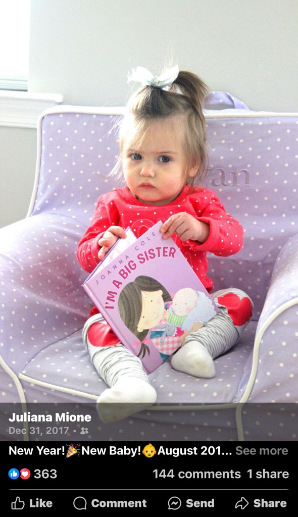 A picture of my daughter at one years old sitting in a purple chair holding a book that says "I'm a big sister" as our pregnancy announcement for baby number two. 