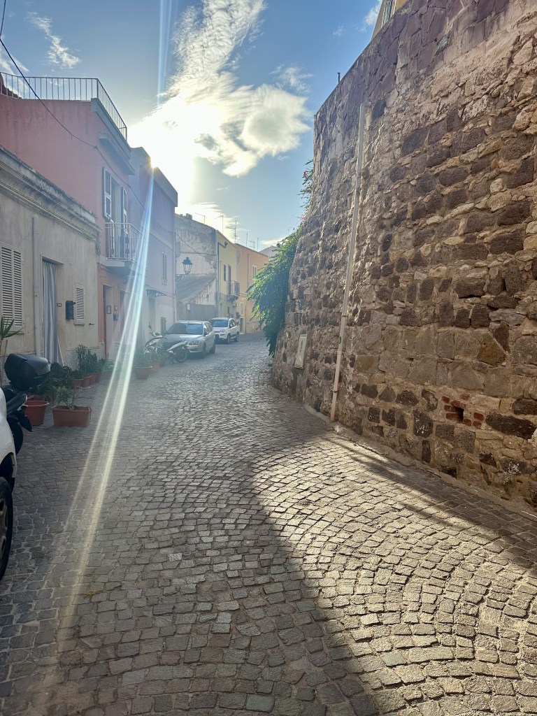 A cobblestone street with a sunbeam sneaking through buildings in Carloforte, an island of San Pietro, Italy. 