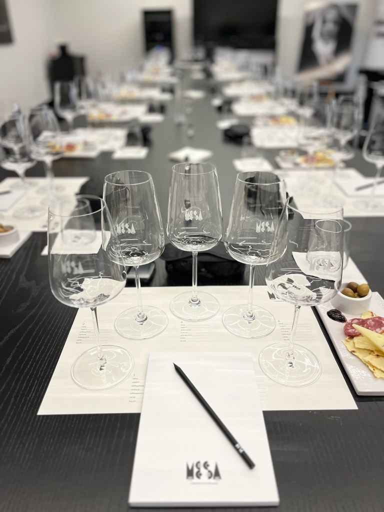 Wine glasses set up for wine tasting on placemat that describes each wine that will be tasted at Cantina Mesa Winery in Sardinia, Italy. There is also a light snack tray to the right to balance out the wine. 