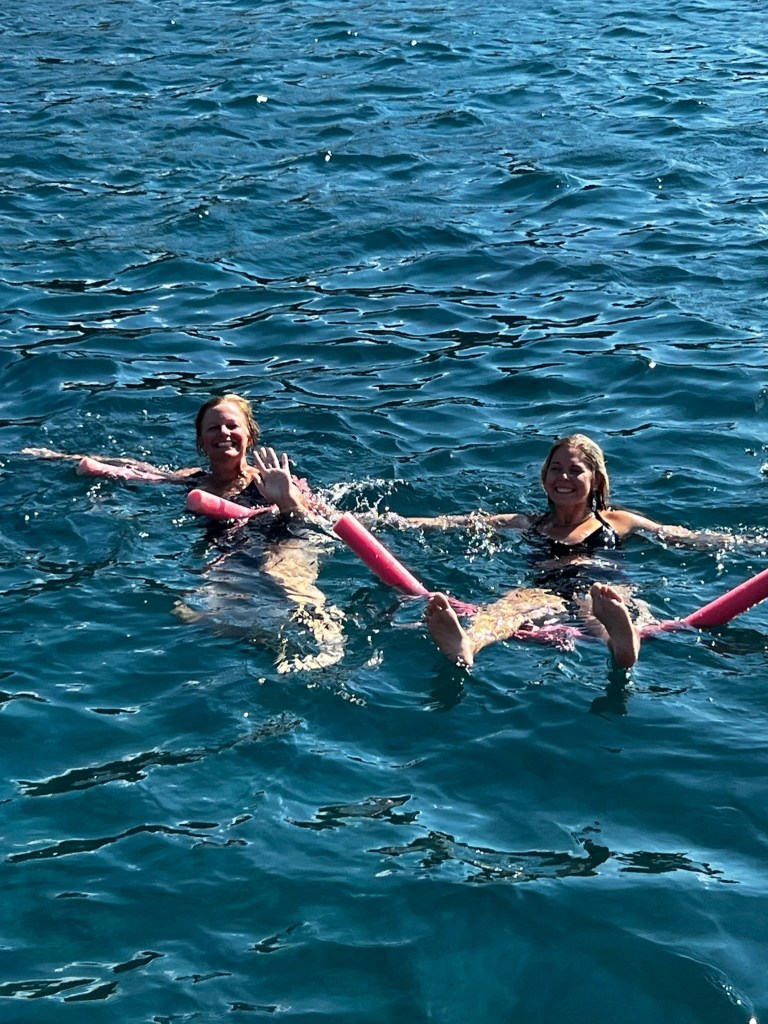 Jules and friend floating on pool noodles in the Mediterranean during a catamaran experience in Santorini, Greece