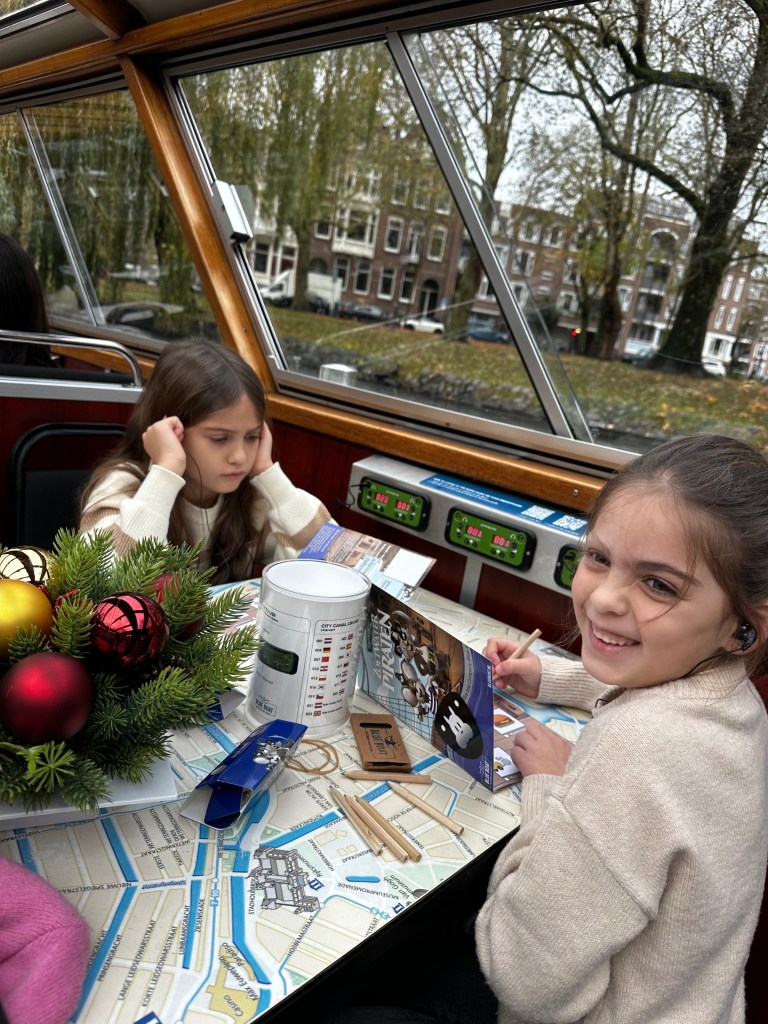 Daughters sitting on canal cruise in Amsterdam with headsets in ears listening to audio while coloring