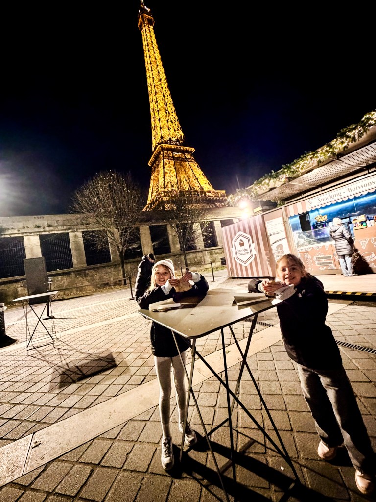 Girls eating Nutella crepes under the Eiffel Tower at night in Paris, France 