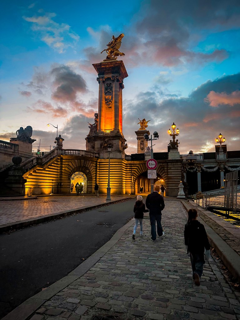 Family walking under one end of the Pont Alexandre III bridge in Paris, France at dusk