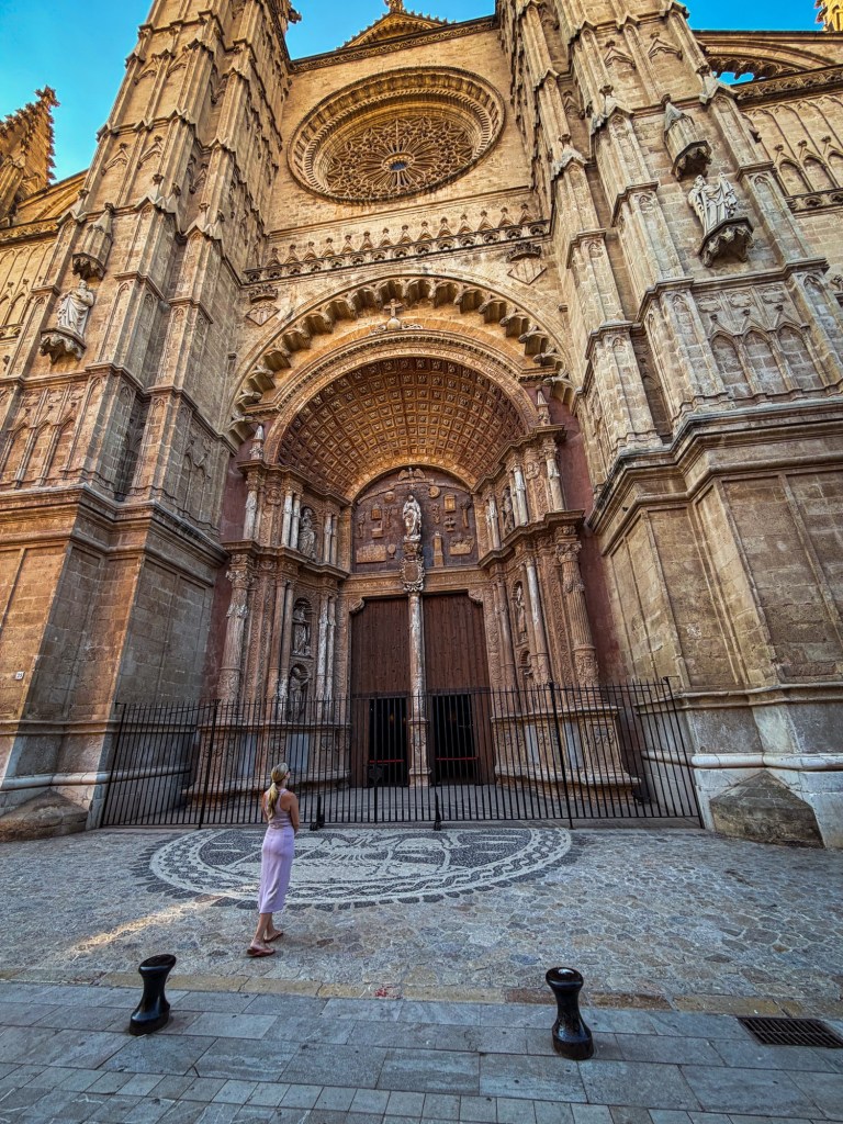Woman in purple dress looking up at The Cathedral of Santa Maria of Palma in Palma de Mallorca, Spain